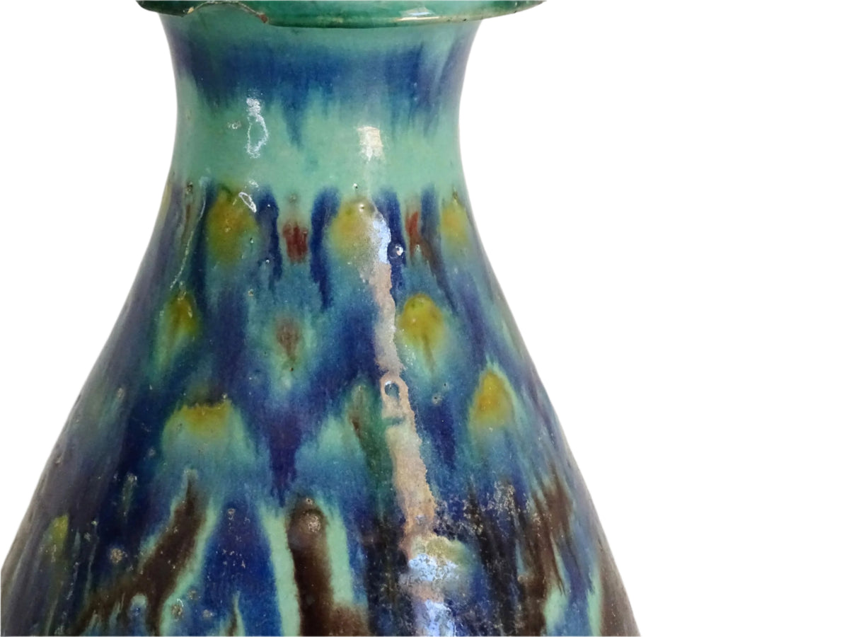 A French vintage ceramic vase lamp base with a bold, multicolored glaze in deep blue, green, and yellow. The organic, dripping pattern covers the surface, giving it a fluid, textured look. The vase has a rounded body that tapers towards a narrower neck, fitted with a brass lamp attachment. It rests on a slightly elevated base.