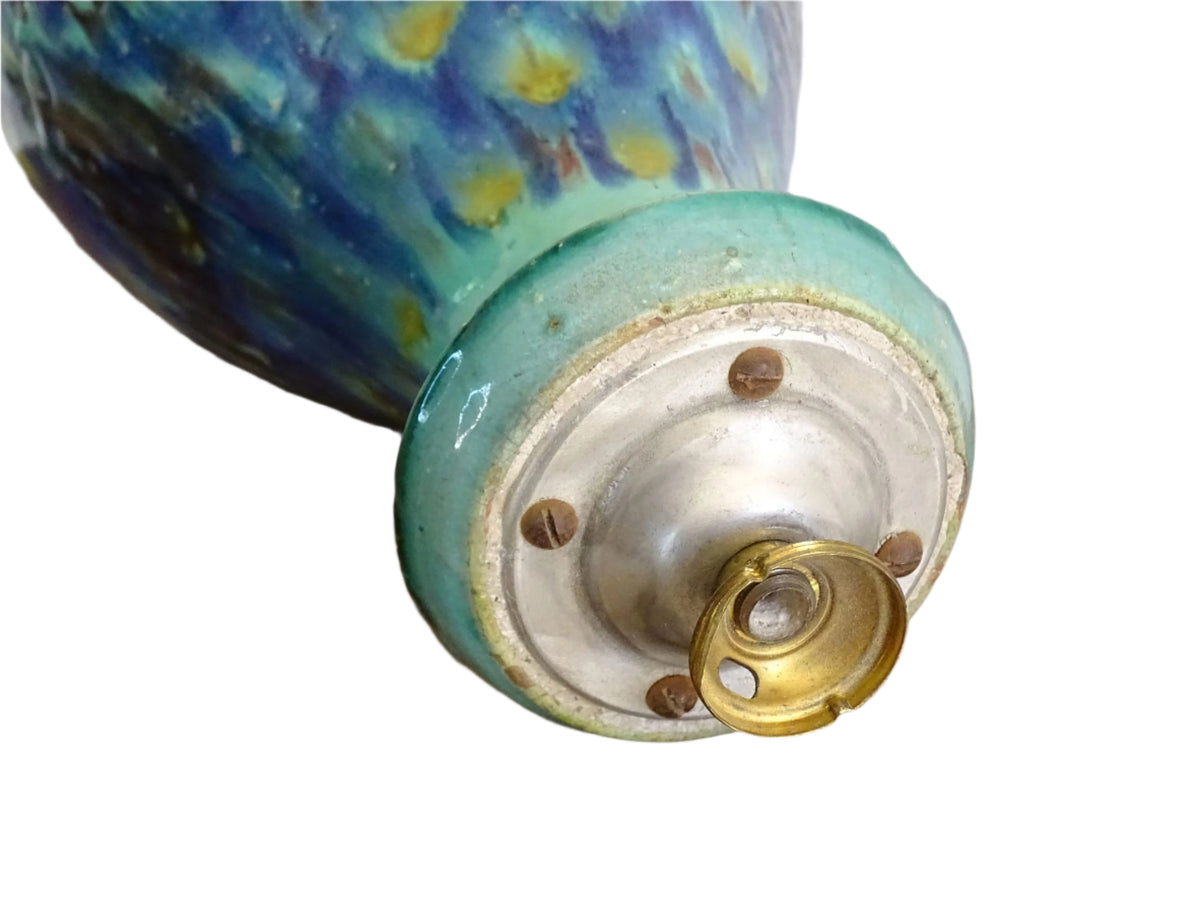A French vintage ceramic vase lamp base with a bold, multicolored glaze in deep blue, green, and yellow. The organic, dripping pattern covers the surface, giving it a fluid, textured look. The vase has a rounded body that tapers towards a narrower neck, fitted with a brass lamp attachment. It rests on a slightly elevated base.