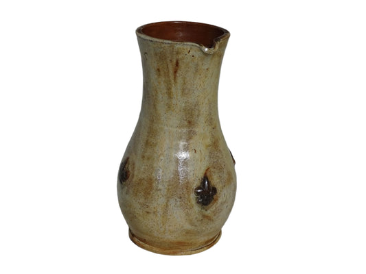 vintage pottery jug with fleur de lys motifs in the style of Roger Guerin. Tall pitcher is glazed in cream, with brown highlights. Display on a sideboard filled with flowers.