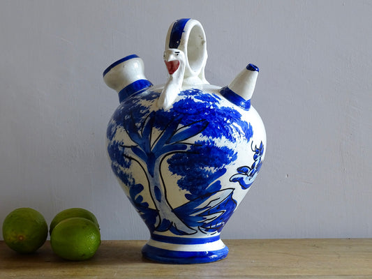 Spanish vintage blue and white ceramic gargoulette. This pottery water pitcher is hand-painted with trees and the figure of an animal. It has a handle to the top with faces to each side, as well as two spouts.
