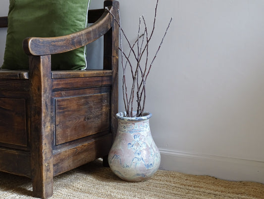 Large French antique ceramic vase with a pink glaze and touches of white and blue. This glazed terracotta vessel has a baluster shape and sits upon a natural jute rug, alongside an antique wooden seat.