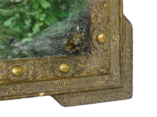 Aged antique French mirror from the Napoleon III period, featuring a frame with stepped corners and finely detailed gesso decoration. The giltwood frame showcases a repeating pattern of oval medallions, floral motifs, and textured cross-hatching.
19th century antique French mirror retains its original mercury glass plate, which shows natural signs of age including foxing and silver loss. The initials "M.J" are on the glass.