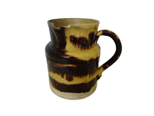 Rustic French antique pottery jug with a brown drip glaze on a yellow glazed background. This old ceramic pitcher has a handle to the side.