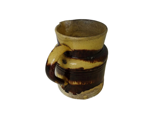 Rustic French antique pottery jug with a brown drip glaze on a yellow glazed background. This old ceramic pitcher has a handle to the side.