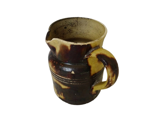 French antique pottery jug with a brown drip glaze on a yellow glazed background. This glazed ceramic pitcher has a handle to the side and would have been used for cooking.