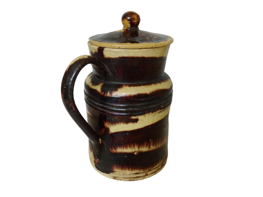 French antique pottery pitcher with a lid. Old ceramic jug with a brown drip glaze on a yellow glazed background.