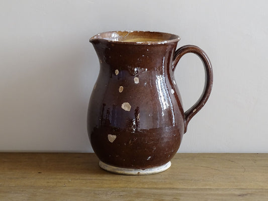 Brown French antique pottery pitcher with yellow glaze interior. Timeworn ceramic jug with handle and spout.