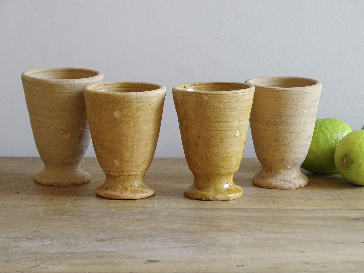Set of four French vintage terracotta goblets. Of the four pottery cups, one has a beautiful yellow glaze, another is partially glazed and the other two are unglazed.