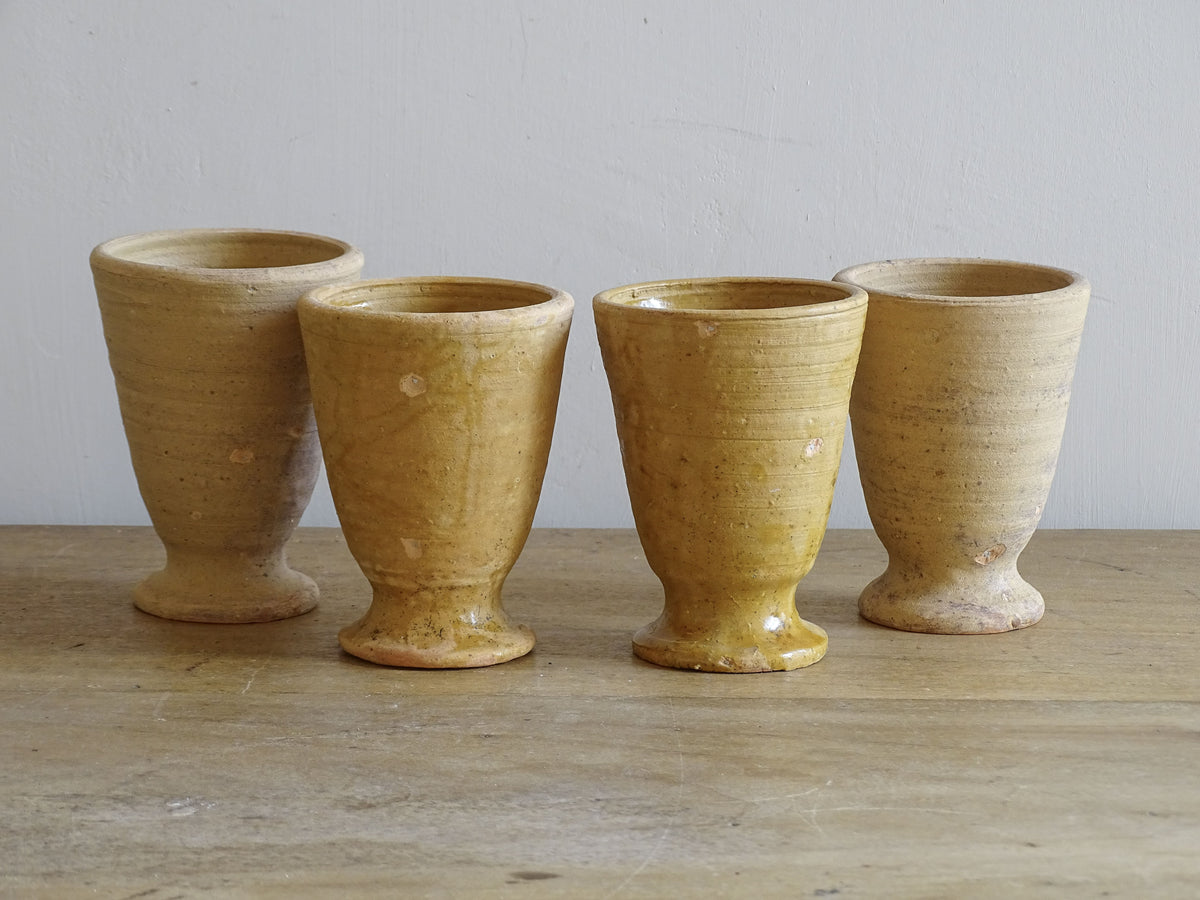 Set of four French vintage terracotta goblets. Of the four pottery cups, one has a beautiful yellow glaze, another is partially glazed and the other two are unglazed.