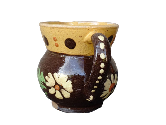 Small French vintage pottery pitcher from Alsace. Ceramic jug with a brown glaze and yellow glazed stripe around the top. It is hand painted with white flowers, green leaves and dots.