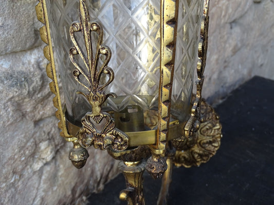 A beautiful French vintage wall light made from gilded metal with a clear cut-glass lantern. The frame has small finials to the top, leaf motifs around the sides, and an ornate scrolling arm. The glass has a diamond pattern.