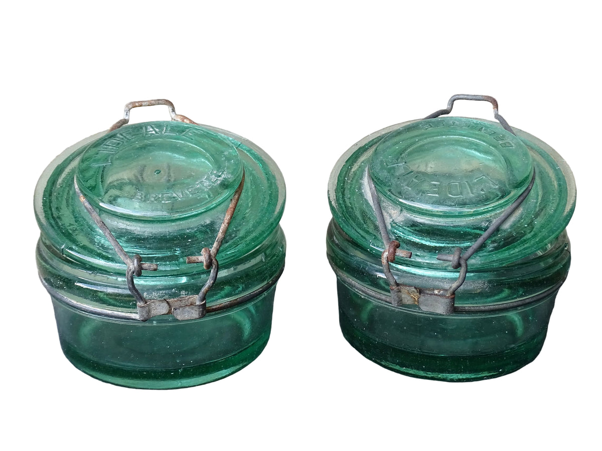 Pair of large French vintage green glass preserving jars by L'Ideale. They feature thick green glass, embossed detailing, and old metal clasps with a naturally aged finish.