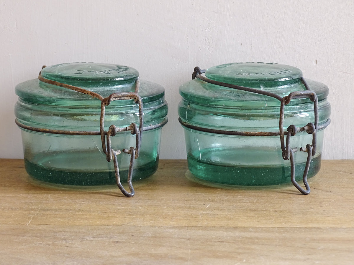 Pair of large French vintage green glass preserving jars by L'Ideale. They feature thick green glass, embossed detailing, and old metal clasps with a naturally aged finish.