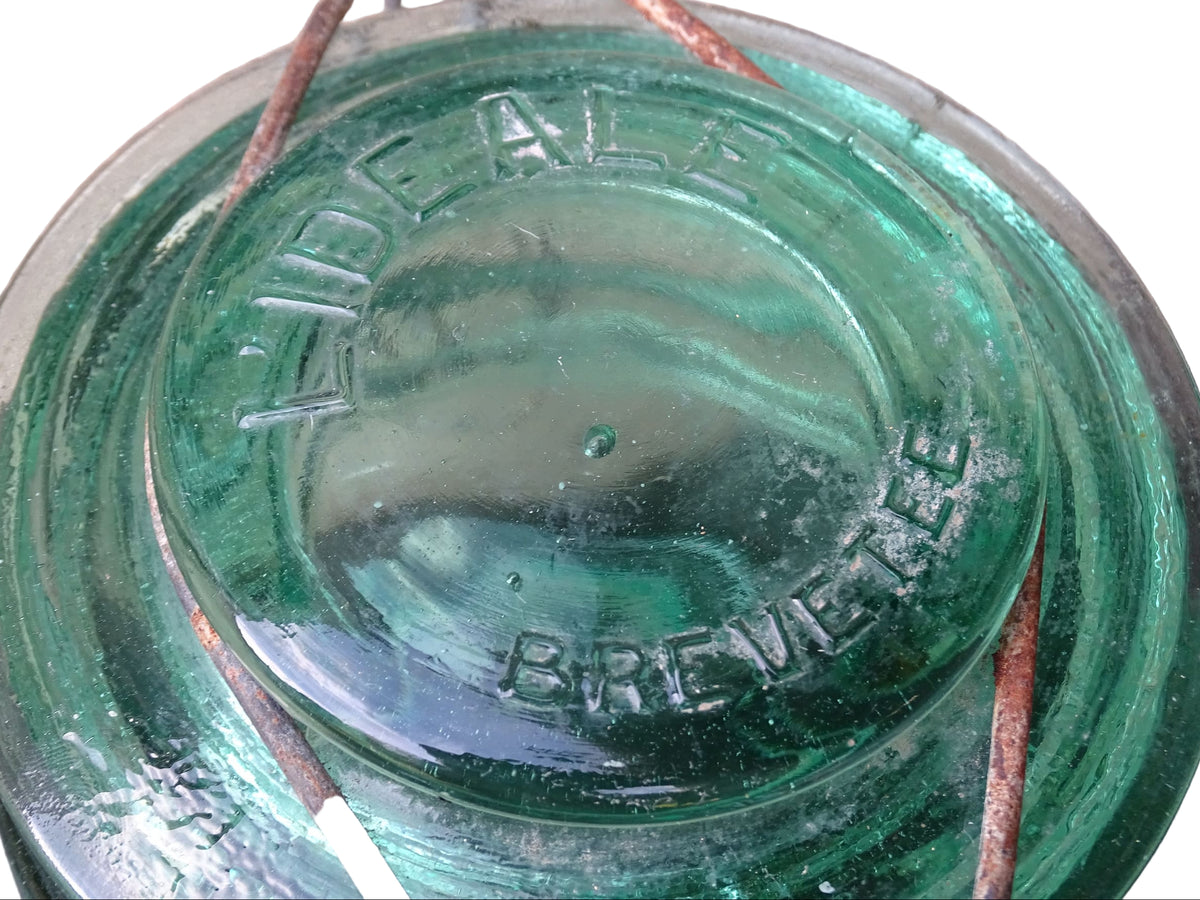 Pair of large French vintage green glass preserving jars by L'Ideale. They feature thick green glass, embossed detailing, and old metal clasps with a naturally aged finish.