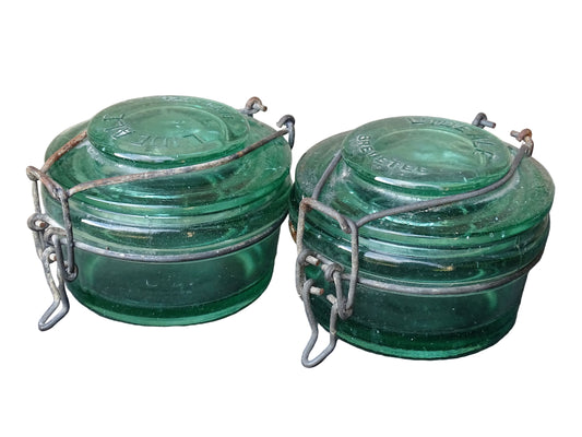 Pair of large French vintage green glass preserving jars by L'Ideale. They feature thick green glass, embossed detailing, and old metal clasps with a naturally aged finish.