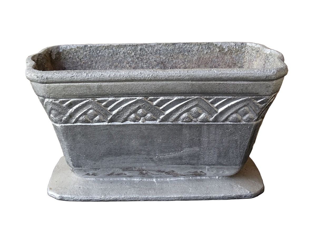 French vintage cast iron planter in silver with a rectangular, flared shape that widens towards the top. It sits on an pedestal-style base. It has a raised geometric border around the upper edge.