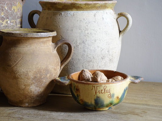 A French vintage ceramic souvenir bowl from Vichy, in the Auvergne region of France. Decorated with hand-applied sponged slip in yellow, green and blue tones. Mid 20th century, with a warm rustic glaze and visible age-related crazing. Pictured alongside rustic French antique pottery including confit pots.