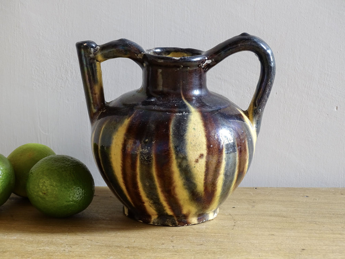 French antique ceramic jug or orjol with striped glaze. Glazed terracotta pitcher with yellow, black and brown glaze.