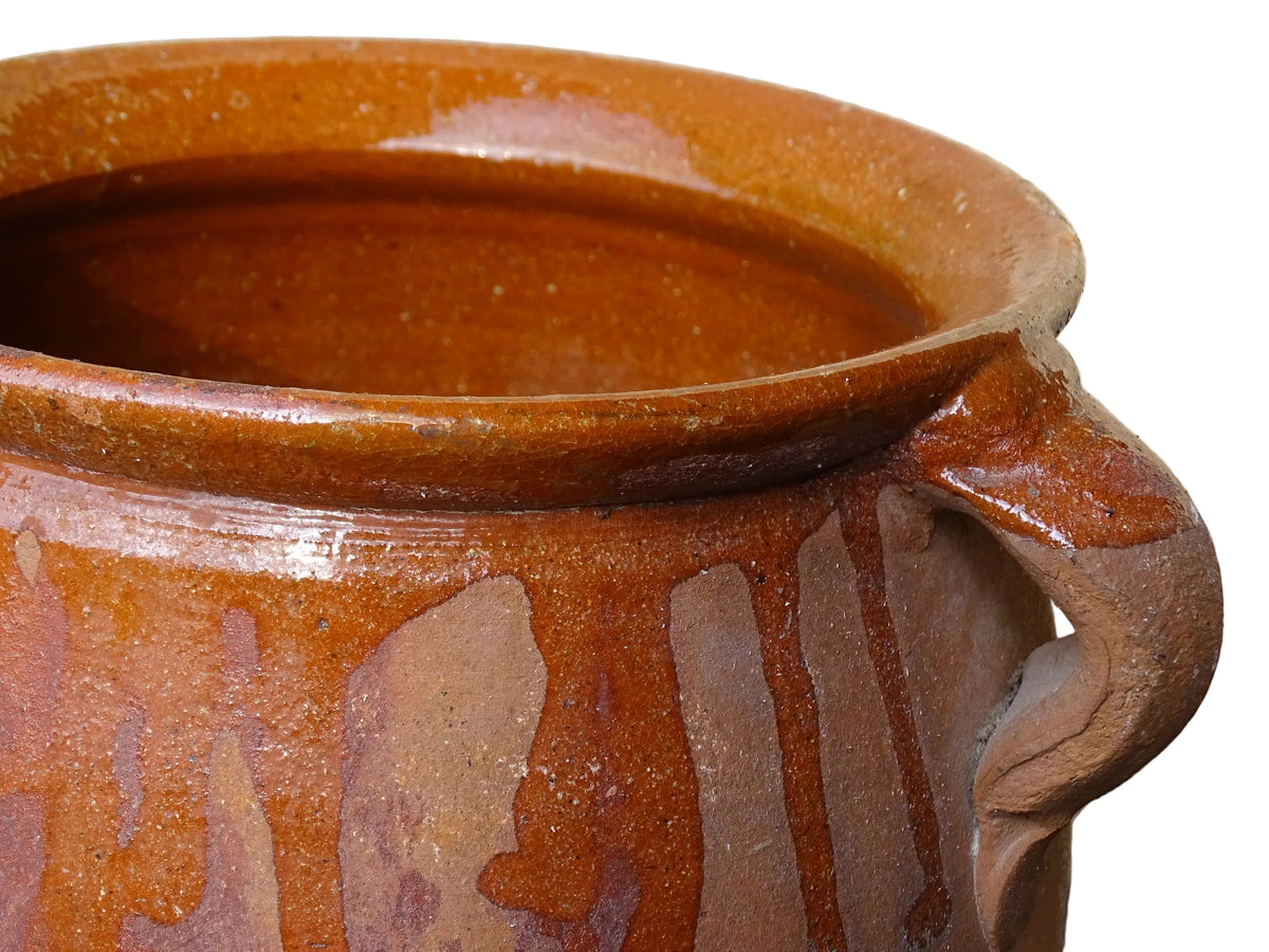 French vintage terracotta pot with orange glaze interior and drip glaze around the sides. Earthenware confit jar with two handles and a curved base.