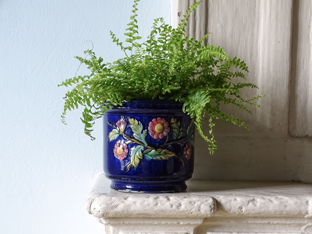 French antique ceramic planter with blue glaze and pink flowers filled with a green fern, pictured on a country house fireplace.