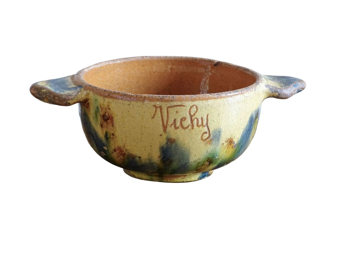 A French vintage ceramic souvenir bowl from Vichy, in the Auvergne region of France. Decorated with hand-applied sponged slip in yellow, green and blue tones. Mid 20th century, with a warm rustic glaze and visible age-related crazing.