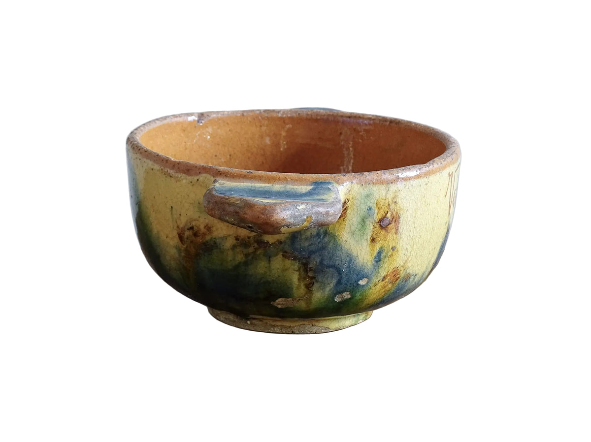 A French vintage ceramic souvenir bowl from Vichy, in the Auvergne region of France. Decorated with hand-applied sponged slip in yellow, green and blue tones. Mid 20th century, with a warm rustic glaze and visible age-related crazing.