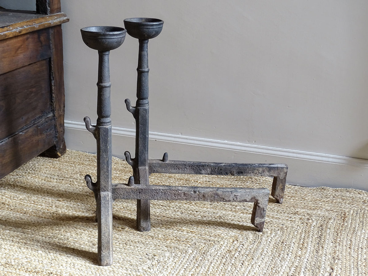 A pair of French antique cast iron andirons or fire dogs, date to the 19th century. They are large and heavy and each have two spit hooks to the front and bowls to the top.