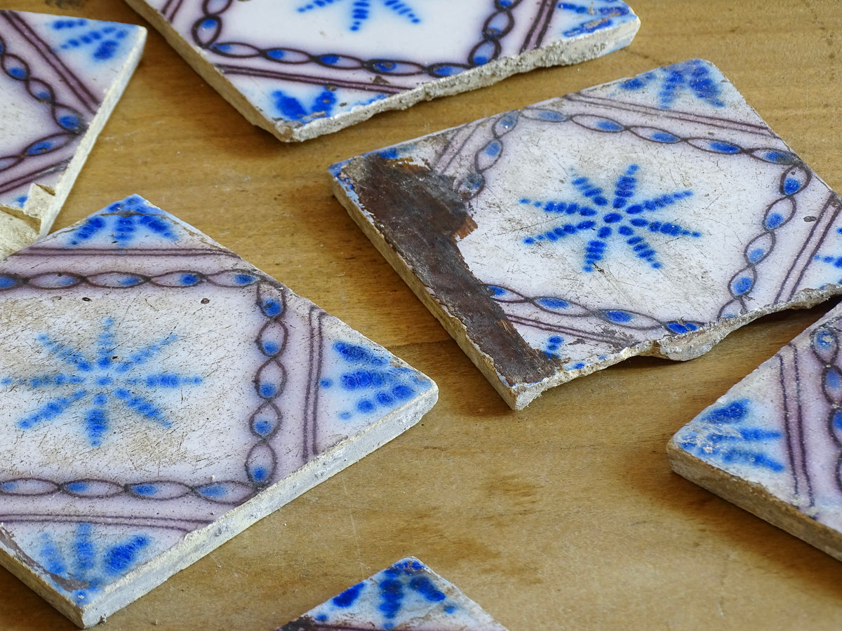 A set of nine French antique Desvres faience tiles in blue & white. These transfer printed, earthenware tiles were manufactured in the late 1900's in Desvres, Northern France. The tiles are back-stamped. Each tile is decorated in cobalt blue on a white tin-glazed ground, centred with a stylised starburst motif and framed within a manganese-purple diamond border.