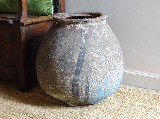 A large, early 19th century French antique terracotta pot, known as a ponne (salting pot), sourced in the Bordeaux region and likely Charentais in origin. This example has a beautifully rounded, generous form with a rolled rim. The surface is particularly special, showing layers of time, wear and historic pigment. Traces of faded blue and earthy tones remain across the body, creating a richly textured patina.