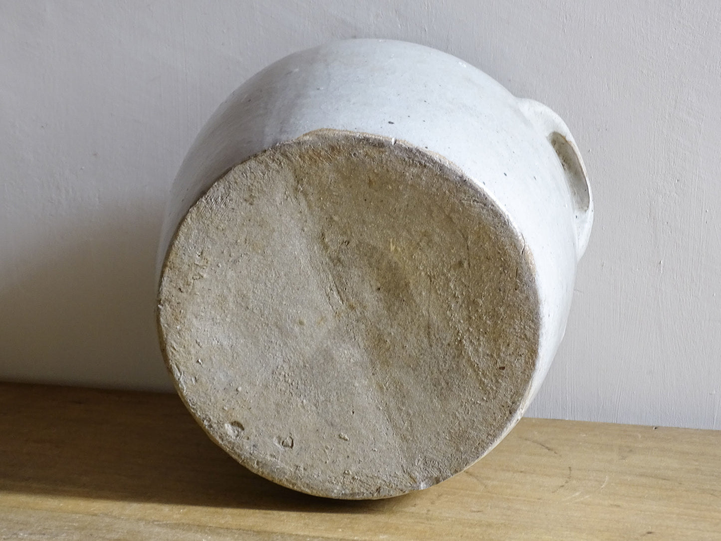 Underside of an antique stoneware jar or French confit pot with a beige glaze and two handles in a rustic country kitchen style.