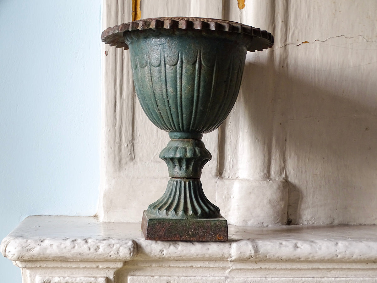 French antique cast iron garden urn with fluted bowl and pedestal base pictured on an old fireplace