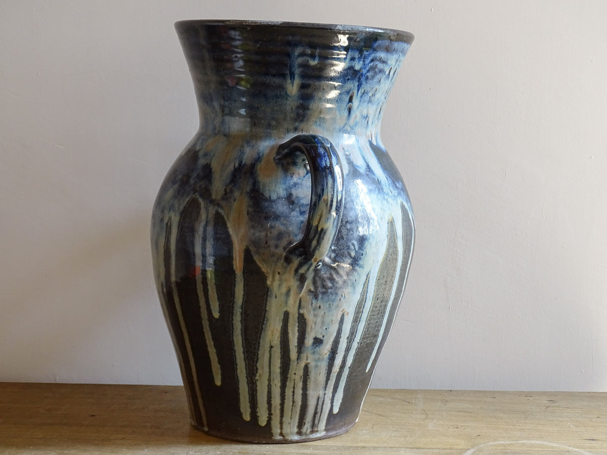 A large vintage studio pottery vase with a blue drip glaze. This stunning ceramic vase has a sculptural amphora form and twin handles, finished in a layered blue drip glaze.