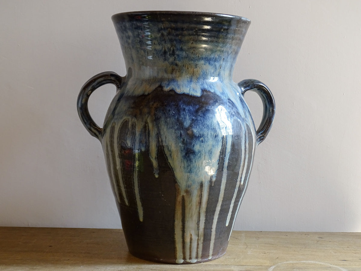 A large vintage studio pottery vase with a blue drip glaze. This stunning ceramic vase has a sculptural amphora form and twin handles, finished in a layered blue drip glaze.