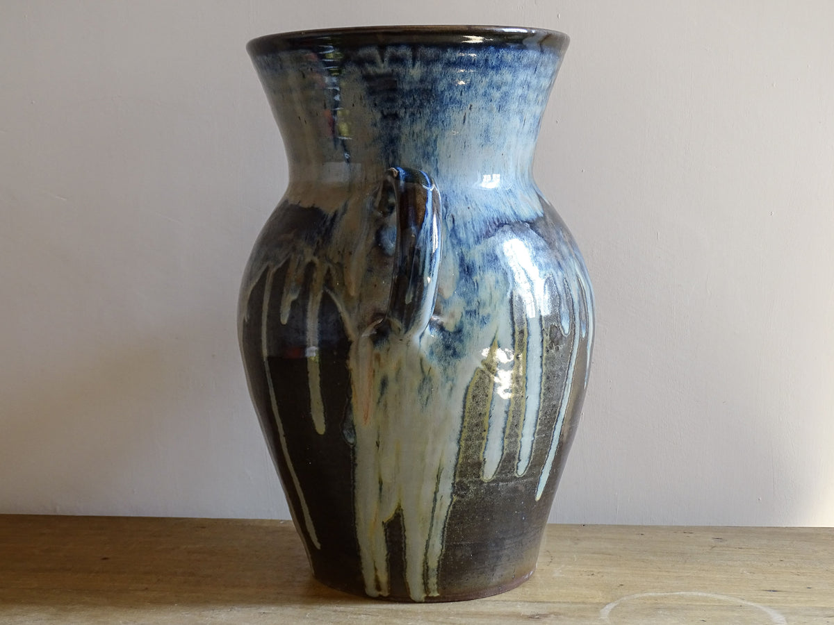 A large vintage studio pottery vase with a blue drip glaze. This stunning ceramic vase has a sculptural amphora form and twin handles, finished in a layered blue drip glaze.