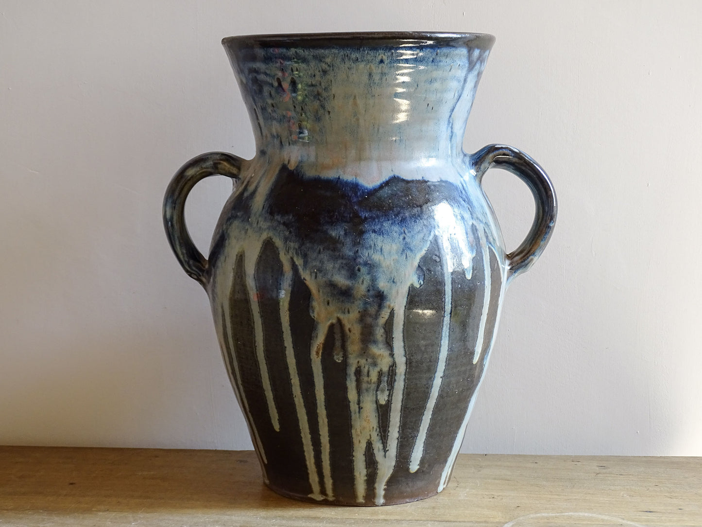 A large vintage studio pottery vase with a blue drip glaze. This stunning ceramic vase has a sculptural amphora form and twin handles, finished in a layered blue drip glaze.