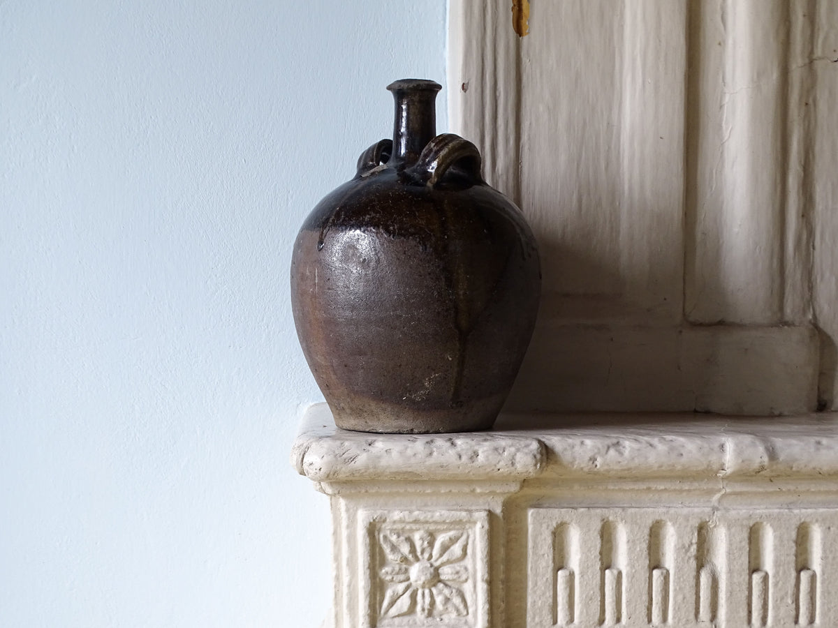 French antique earthenware pitcher with a dark brown glaze, pictured on a country house fireplace mantel