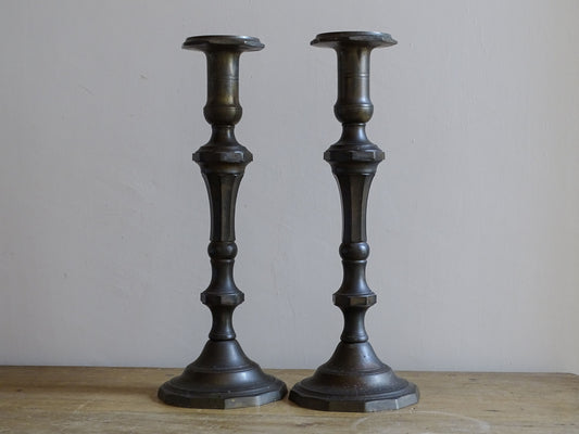 Full-length view of a matching pair of large antique candlesticks in dark patinated metal