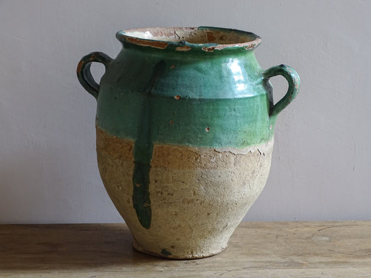 Antique French confit pot with unusual turquoise-green and mustard-yellow glaze, twin handles and a heavily weathered earthenware surface.
