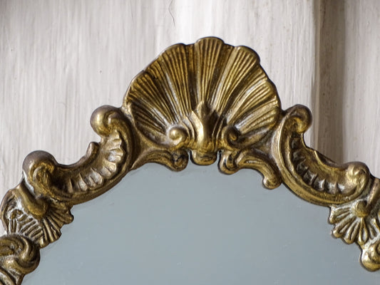 Close-up of the decorative scallop shell crest and scrolling brasswork on a vintage French Rococo-style dressing table mirror
