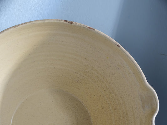 Detail of the interior and rim of a French antique tian bowl with pale yellow glaze, small rim chips and a traditional pouring lip.