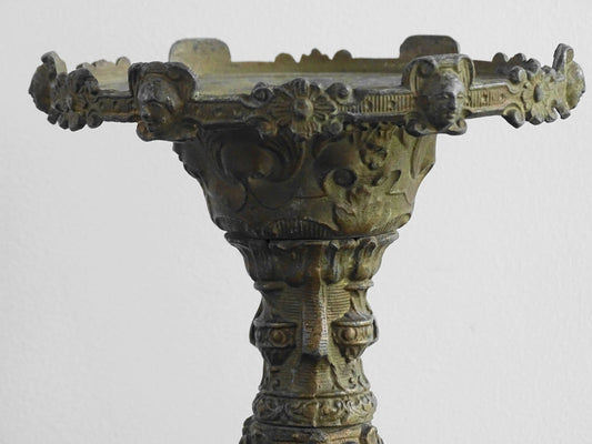 Ornate French antique cast iron candle holder with tripod base and decorated with cherubs.