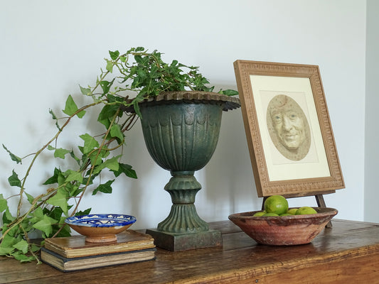 French antique cast iron urn with antique artwork and ceramic bowls on a sideboard in a French country home