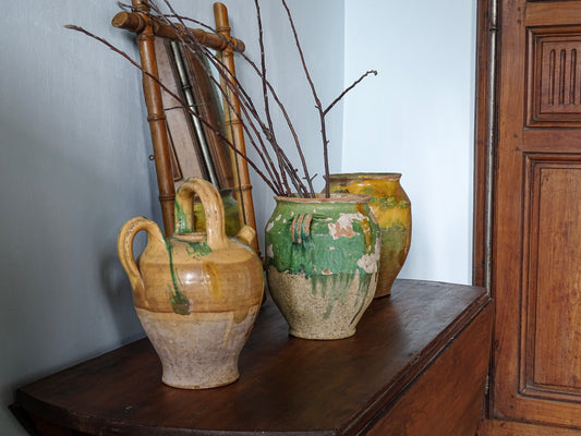 French antique ceramic pitcher with a yellow glaze alongside French confit pots with yellow and green glazes on a table in a French country interior