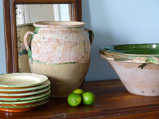 Antique French confit pot alongside plates and a tian bowl with green glaze in a French country interior