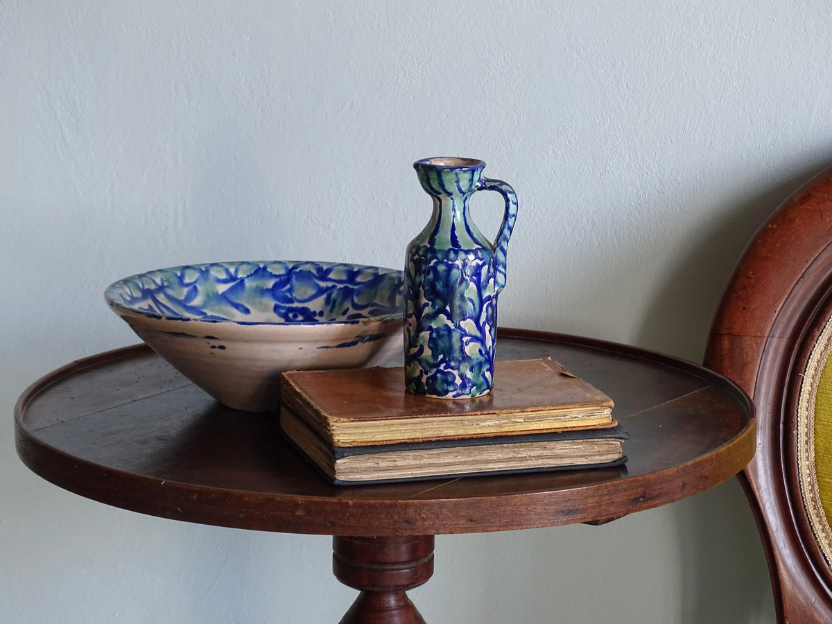 Spanish antique fajalauza pottery bowl with green and blue glaze and Fajalauza pitcher on a table with antique books.
