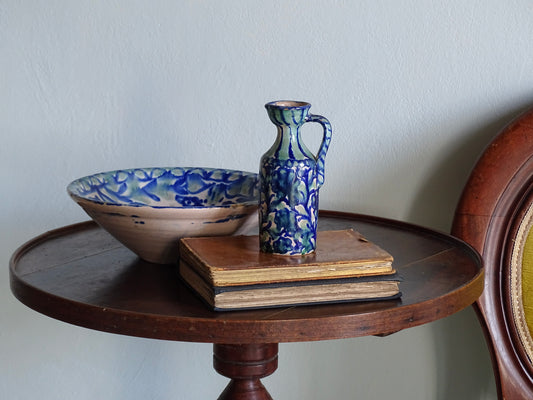 Spanish antique fajalauza pottery bowl with green and blue glaze and Fajalauza pitcher on a table with antique books.