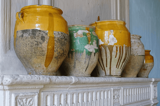 Antique French confit pots with yellow and green glaze on a stone fireplace in a French country home