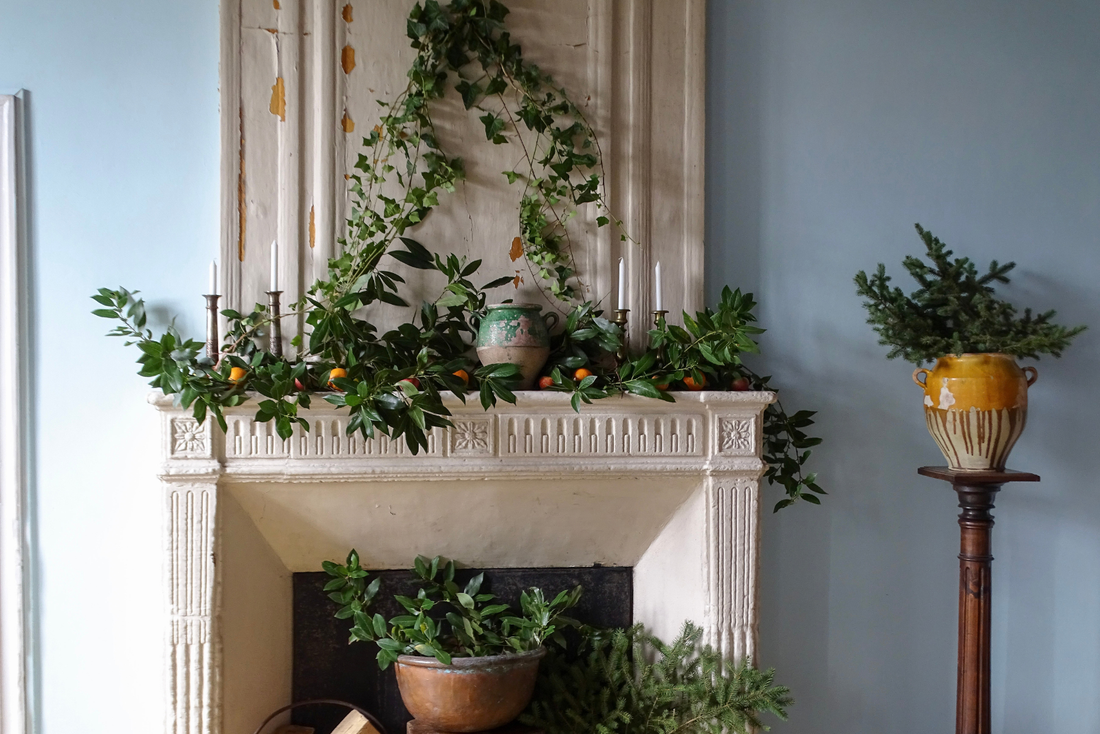 French country Christmas interior with antique fireplace, greenery, confit pots and candlesticks.