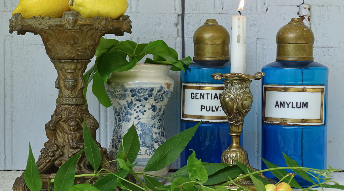 Antique French apothecary bottles with blue glass, brass tops and porcelain labels. Next to an antique Italian albarello medicine jar and two antique candle holders. 