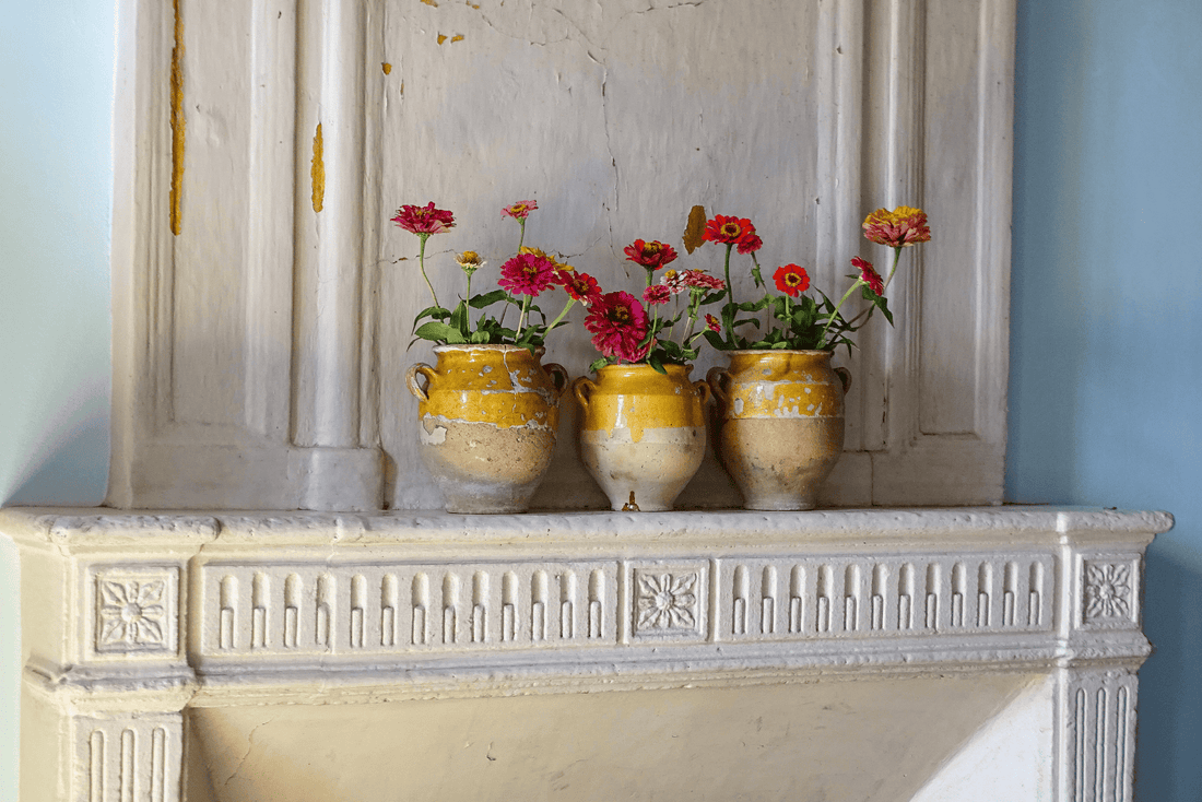 Three antique French yellow confit pots filled with garden flowers on an old fireplace mantel